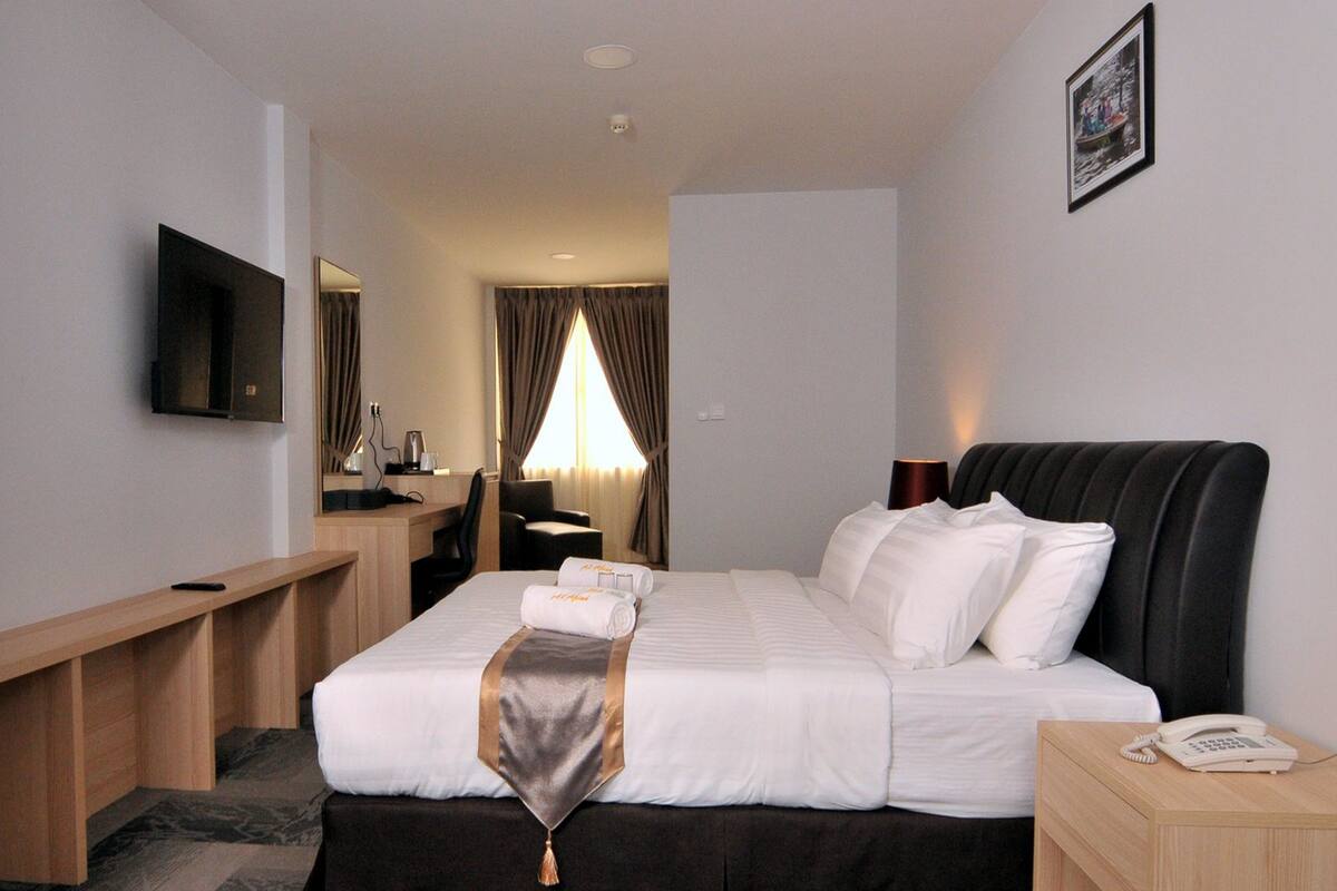 A hotel room with a bed, bedside table, desk, chair, and a television.
