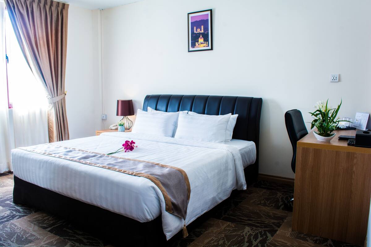 A hotel room with a large bed, a desk, and a potted plant.