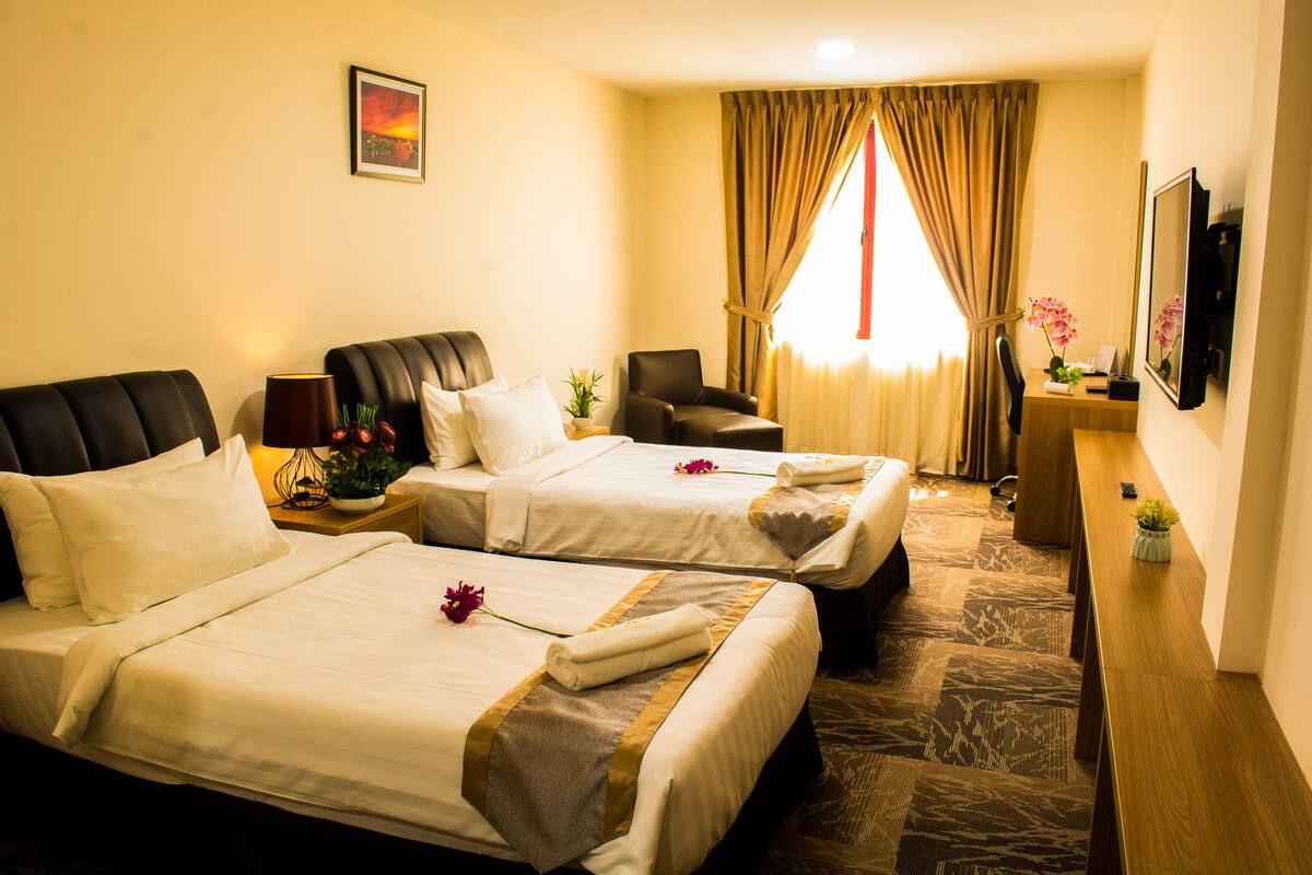 A hotel room with two beds, a desk, a chair, a TV, and a window with curtains.