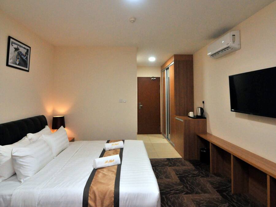 A hotel room with a bed, bedside lamps, a flat-screen TV, a desk, and an air conditioning unit.