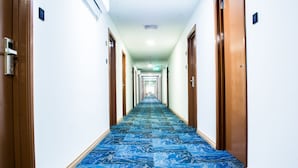Un lungo e stretto corridoio d'hotel con tappeto a motivi, porte in legno e parete bianca.