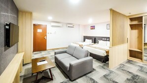 Una camera d'albergo con un divano grigio, un tavolo in legno, un letto con biancheria bianca e un armadio.