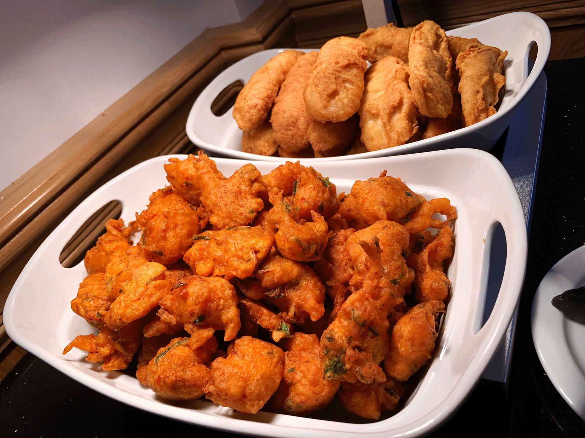 Two white plates filled with golden-brown fried food items, likely fritters, on a kitchen counter.