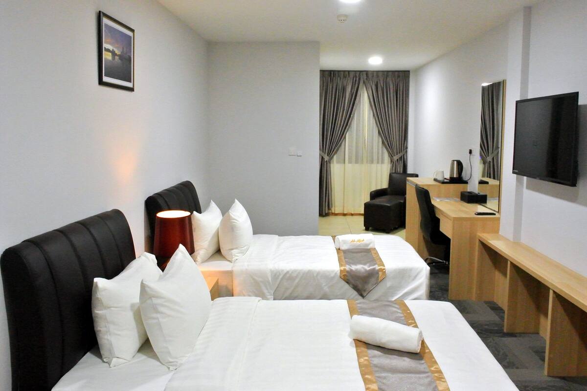 A hotel room with two beds, a desk, a chair, a TV, and a window with curtains.