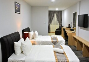 Quarto de hotel com duas camas, uma escrivaninha, uma cadeira, uma televisão e uma janela com cortinas.