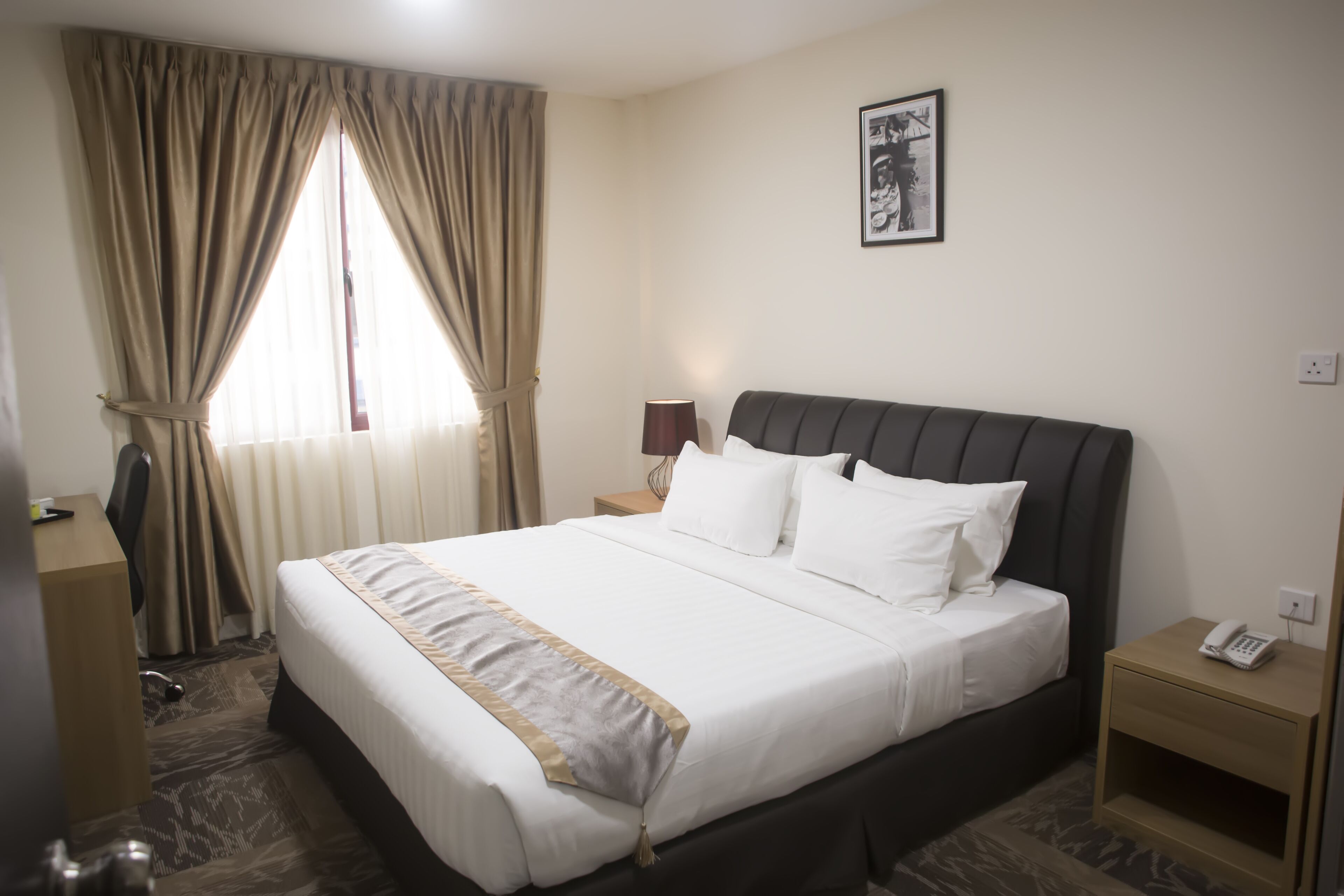 A hotel room with a large bed, a bedside table with a lamp, a desk, and a chair.