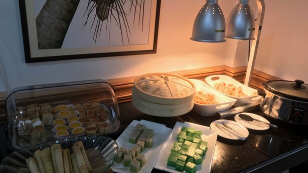 Un tavolo da buffet con diversi piatti, tra cui uno con cubetti verdi, uno con cubetti gialli e uno con cubetti bianchi. Si vedono anche un piatto con involtini e uno con un coperchio.