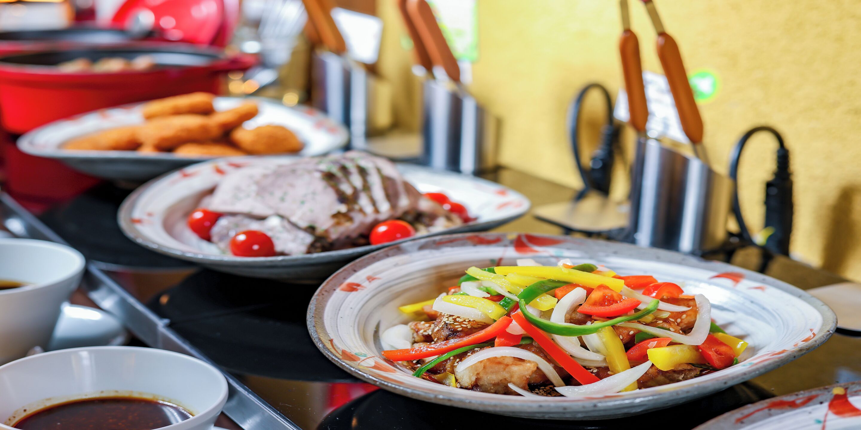 A variety of dishes on a buffet table, including a plate with sliced meat and vegetables, a plate with a red sauce, and a bowl of soup.