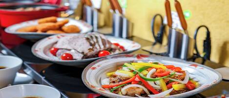 A variety of dishes on a buffet table, including a plate with sliced meat and vegetables, a plate with a red sauce, and a bowl of soup.