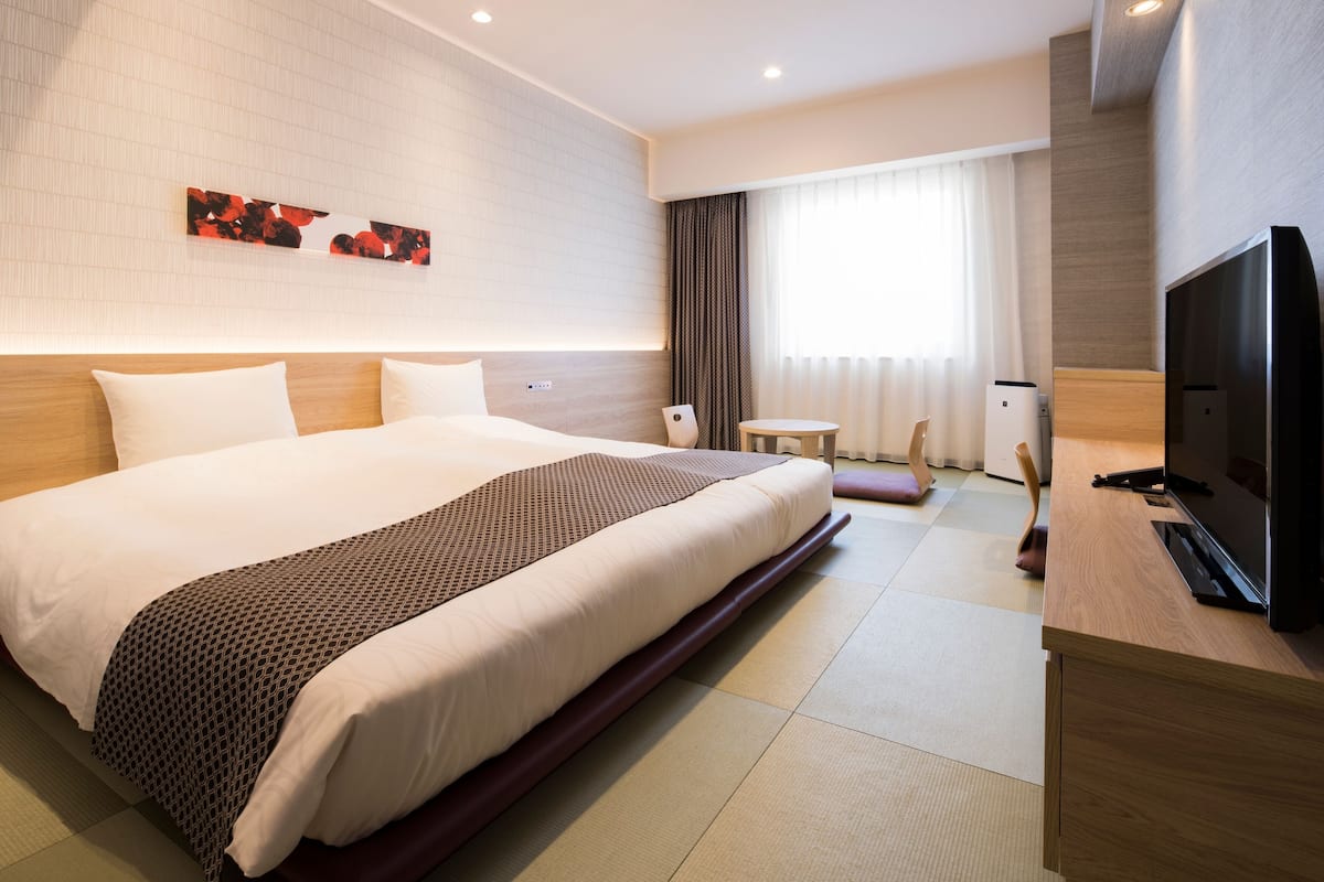 Ein Hotelzimmer mit einem großen Bett, einem Flachbildfernseher, einem Holztisch und einem Fenster mit Vorhängen.