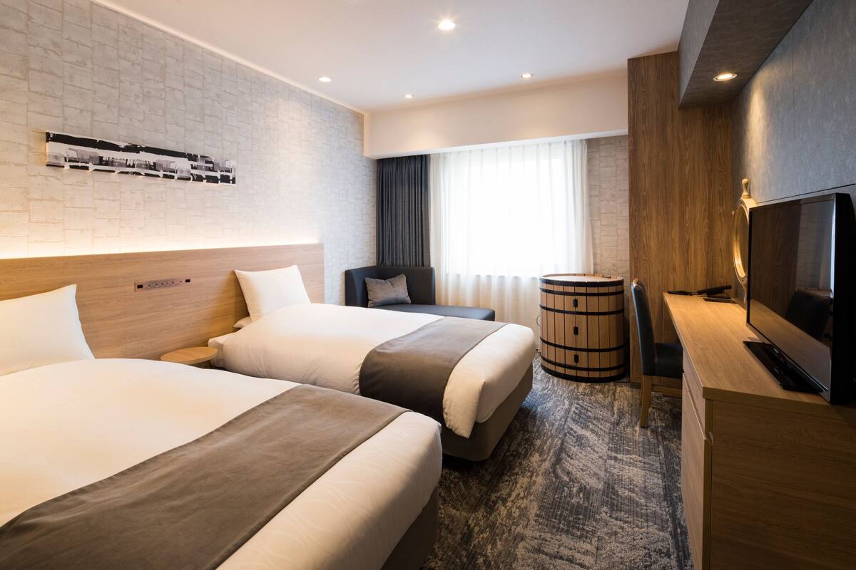 Ein Hotelzimmer mit zwei Betten, einem Schreibtisch, einem Fernseher und einer Wand mit Holzverkleidung.