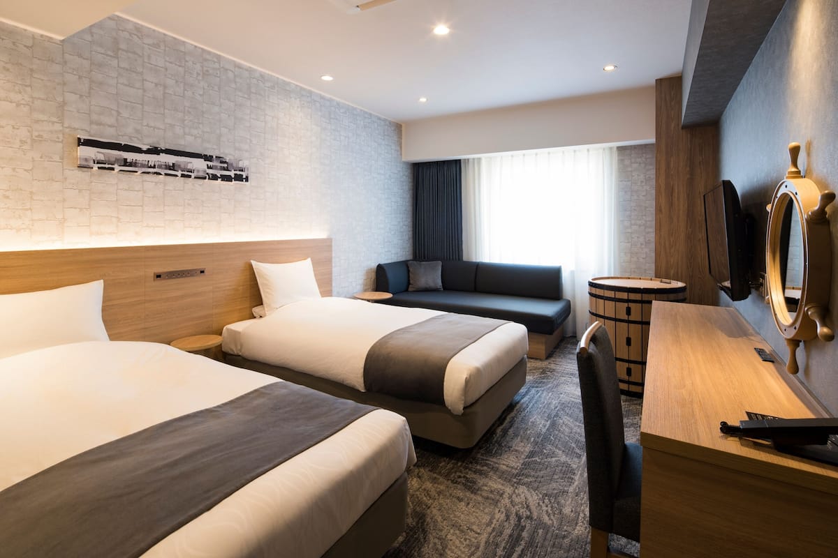 Ein Hotelzimmer mit zwei Betten, einer Couch, einem Schreibtisch und einem Spiegel.