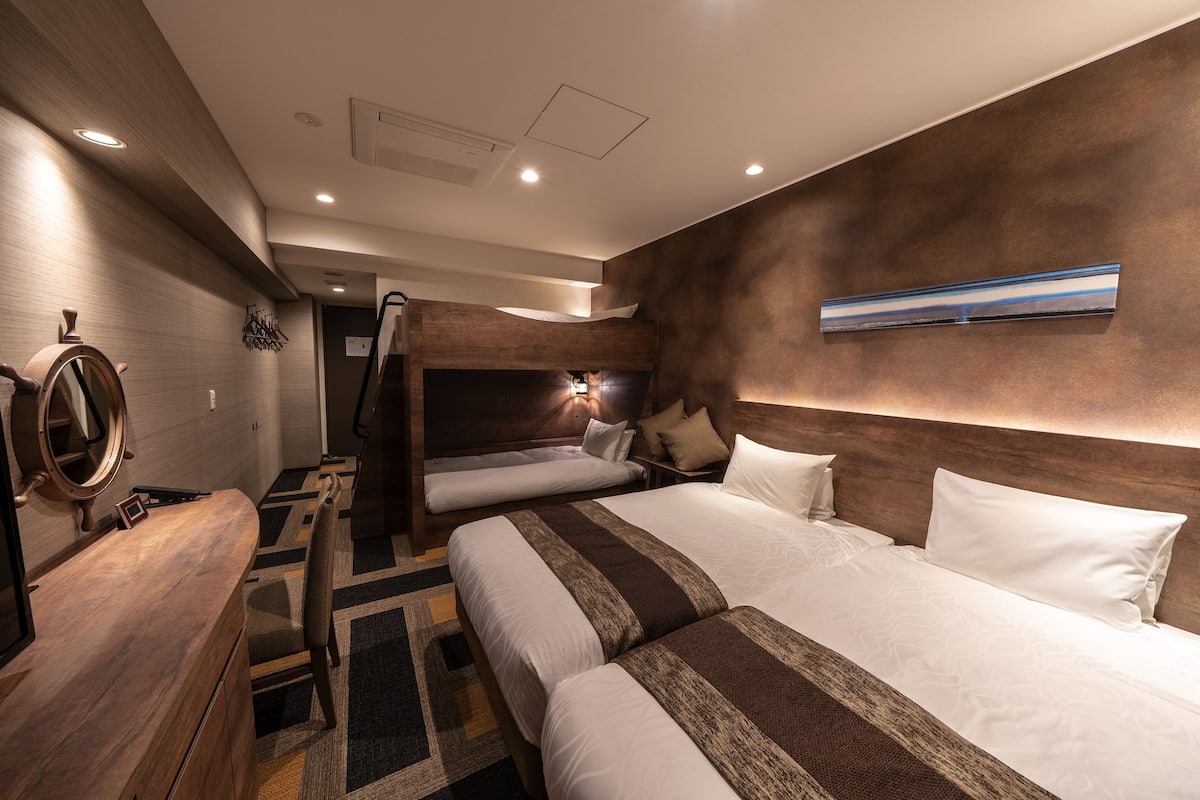 Ein Hotelzimmer mit zwei Betten, einem Holztisch, einem Schiffswellenrad und einer wandmontierten Lampe.