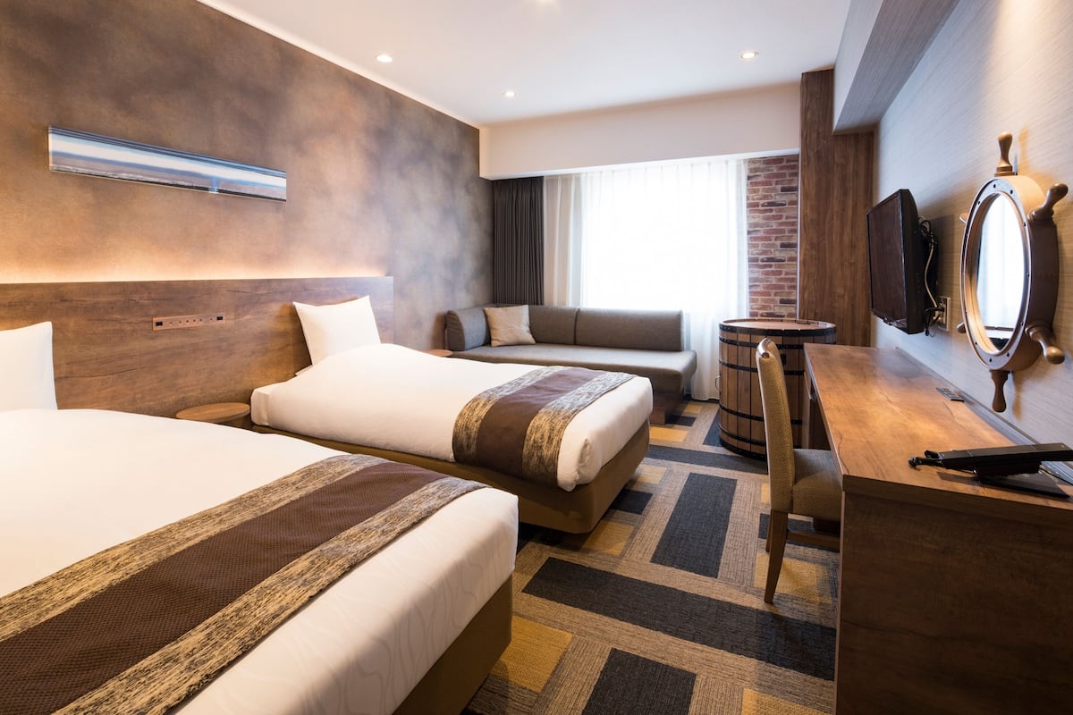 Ein Hotelzimmer mit zwei Betten, einem Schreibtisch, einem Stuhl, einem runden Tisch, einem Spiegel und einem Fernseher.