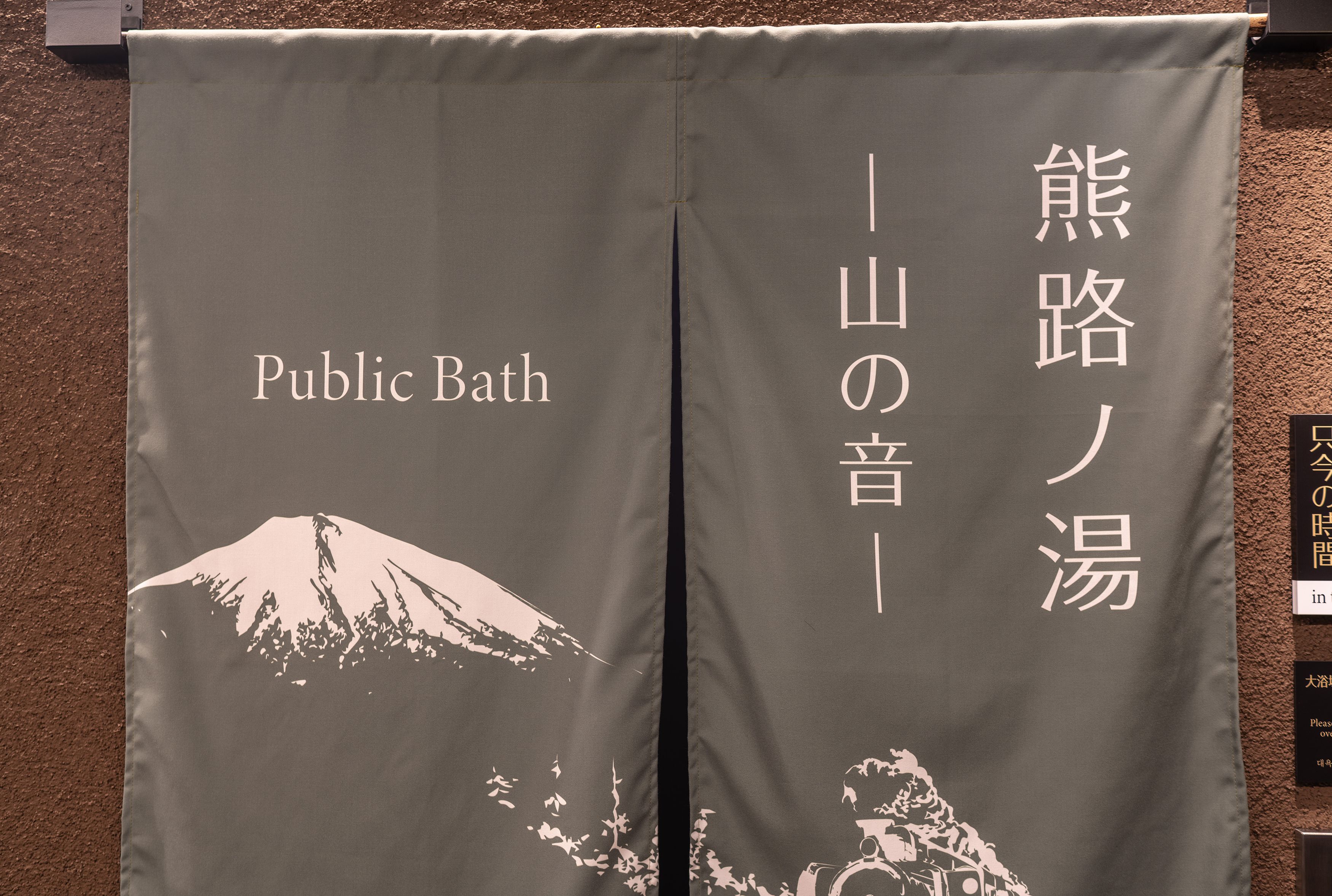 Ein Banner mit Text und einer Bergdarstellung, wahrscheinlich eine Kennzeichnung für einen Ort oder eine Einrichtung im Zusammenhang mit einem öffentlichen Badehaus.