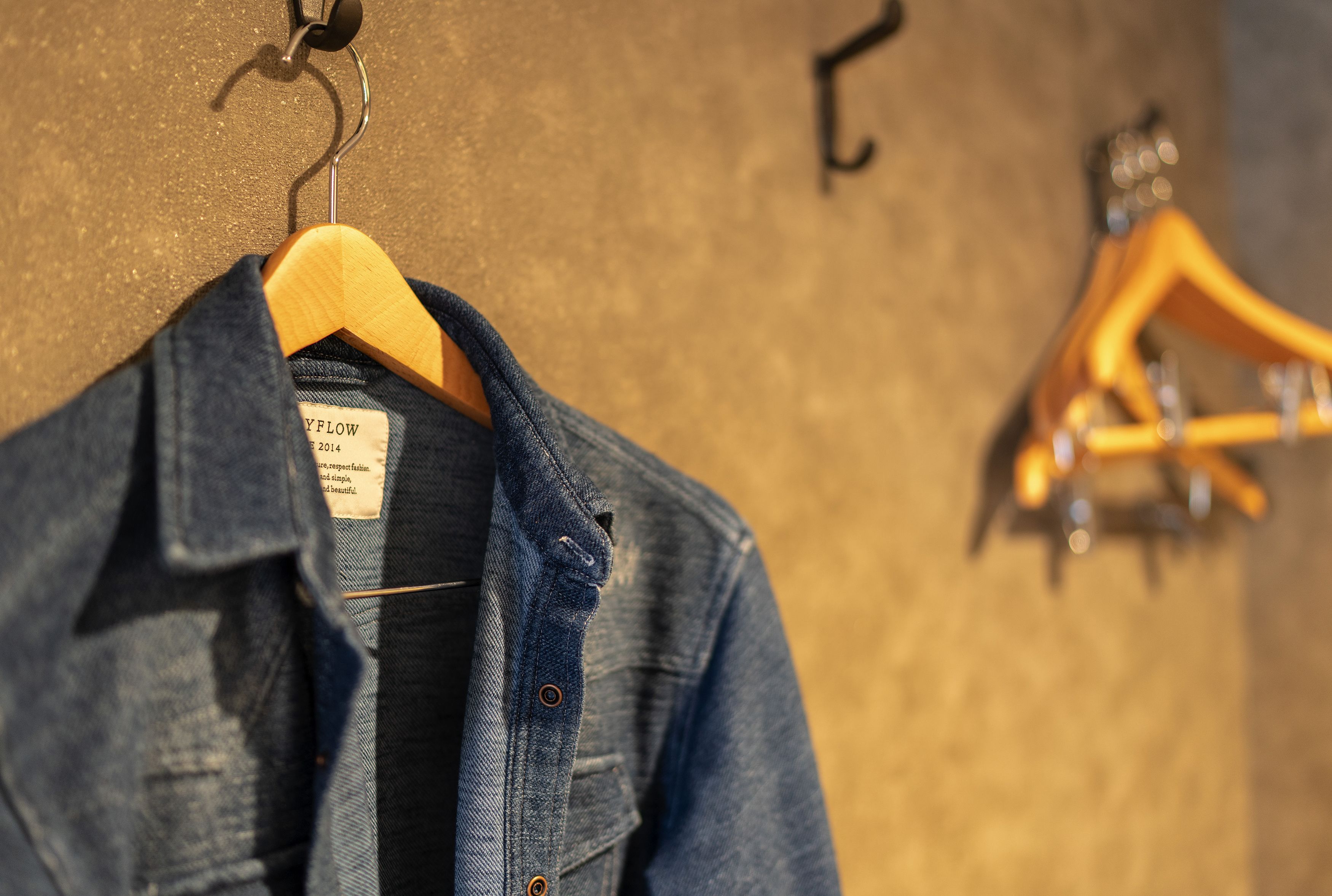 Een denimjas aan een houten kapstok met een label, en een gitaar hangt op een andere kapstok op de achtergrond.