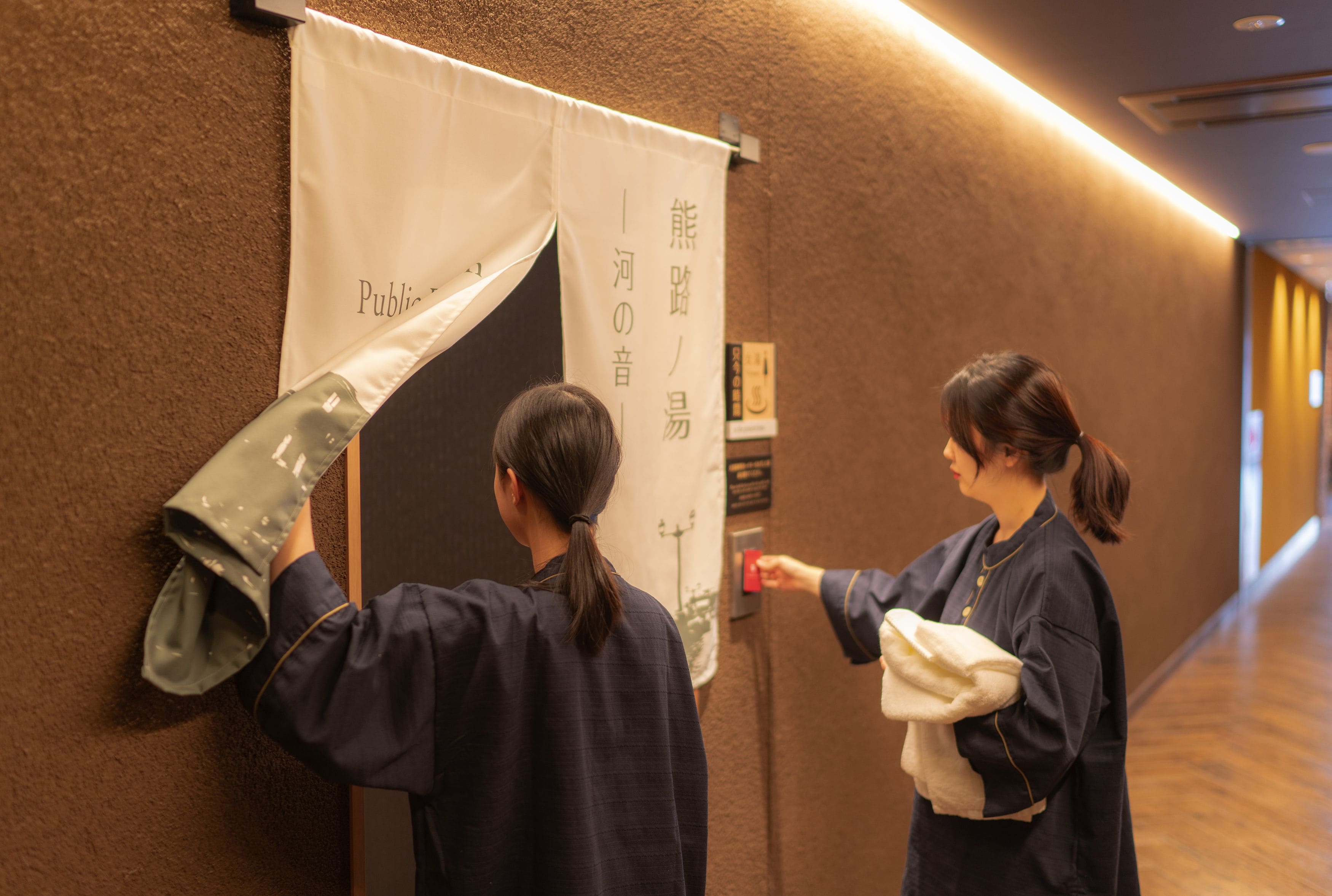 Two individuals adjusting a banner in a hallway with a wooden floor and a textured wall.