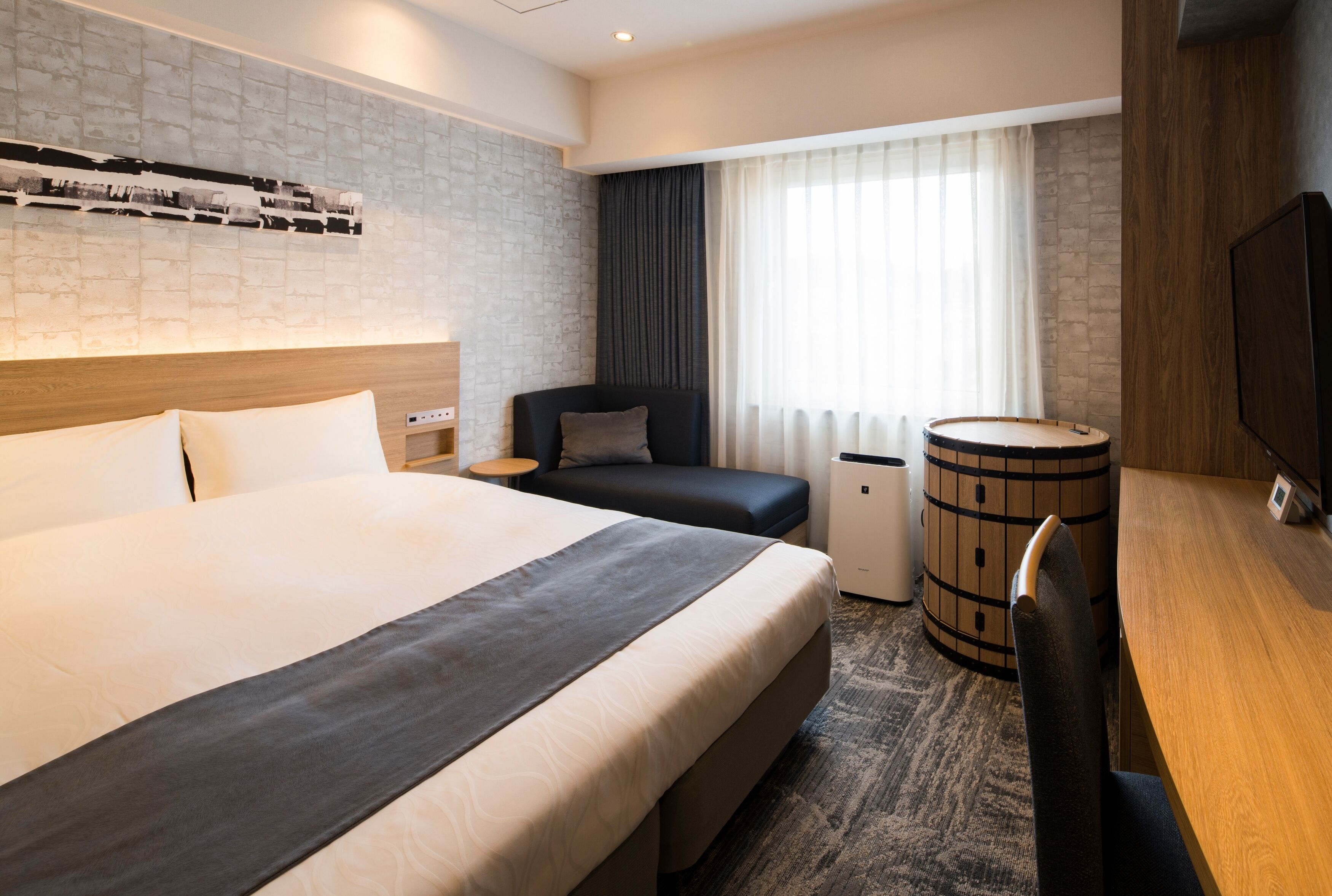 A hotel room with a large bed, a desk, a chair, a small table, a TV, and a window with curtains.
