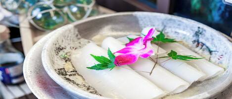 A bowl with white cylindrical items, possibly food, garnished with a pink flower and green leaves.
