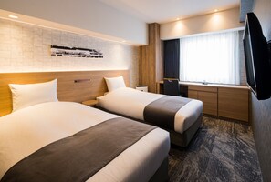 A hotel room with two beds, a TV, a window with curtains, and a brick wall with a photo display.