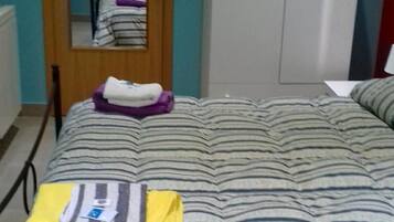Quarto com colcha listrada, guarda-roupa e espelho refletindo uma pessoa.