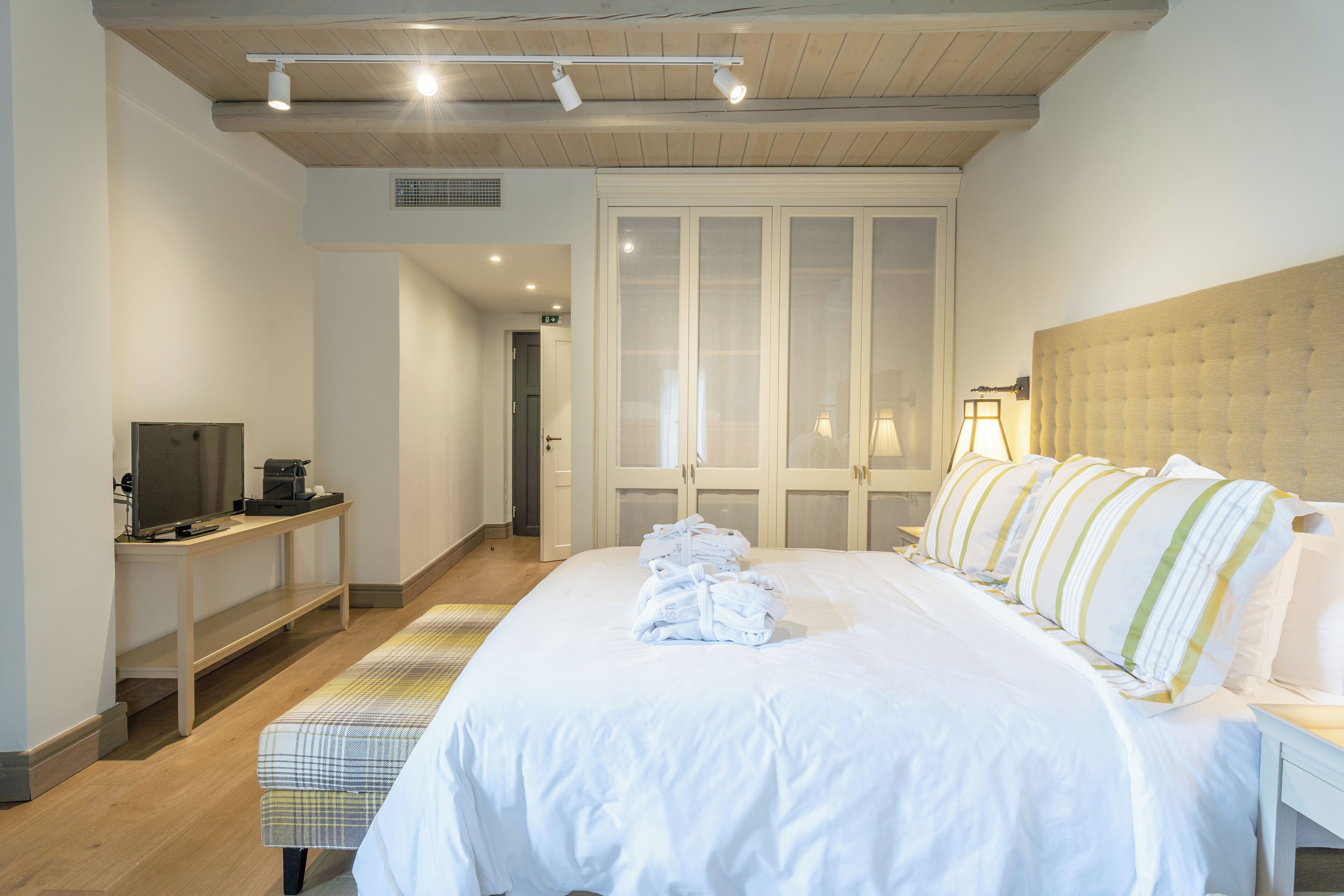 Una habitación de hotel con una cama grande, un escritorio con televisor y un armario con puertas de cristal.