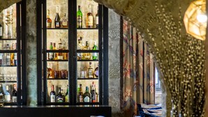 Una zona de bar con pared de piedra, estantes llenos de botellas de licor y un espacio de estar con sofá y sillones.