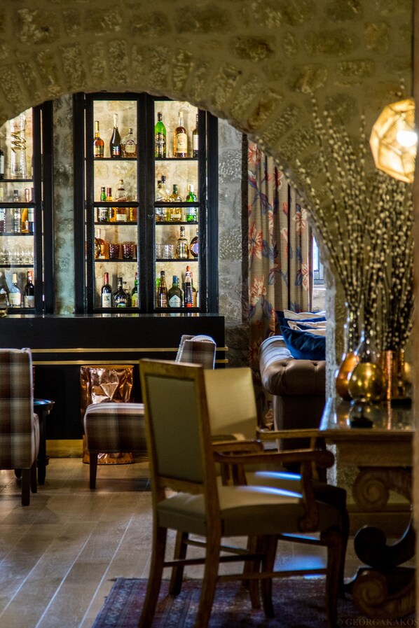 Una zona de bar con pared de piedra, estantes llenos de botellas de licor y un espacio de estar con sofá y sillones.