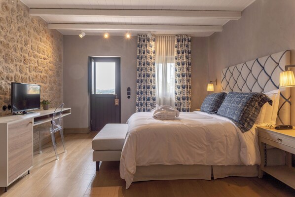Un dormitorio con cama, escritorio, silla, televisor y ventana con cortinas.