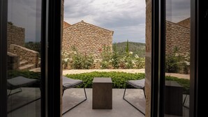 Vista a través de un vidrio de una construcción de piedra, con una mesa cuadrada y dos sillas en primer plano.
