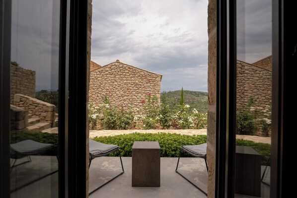 A view through a glass door of a stone building with a square table and two chairs in the foreground. - Alistos Hotel (East Mani)
