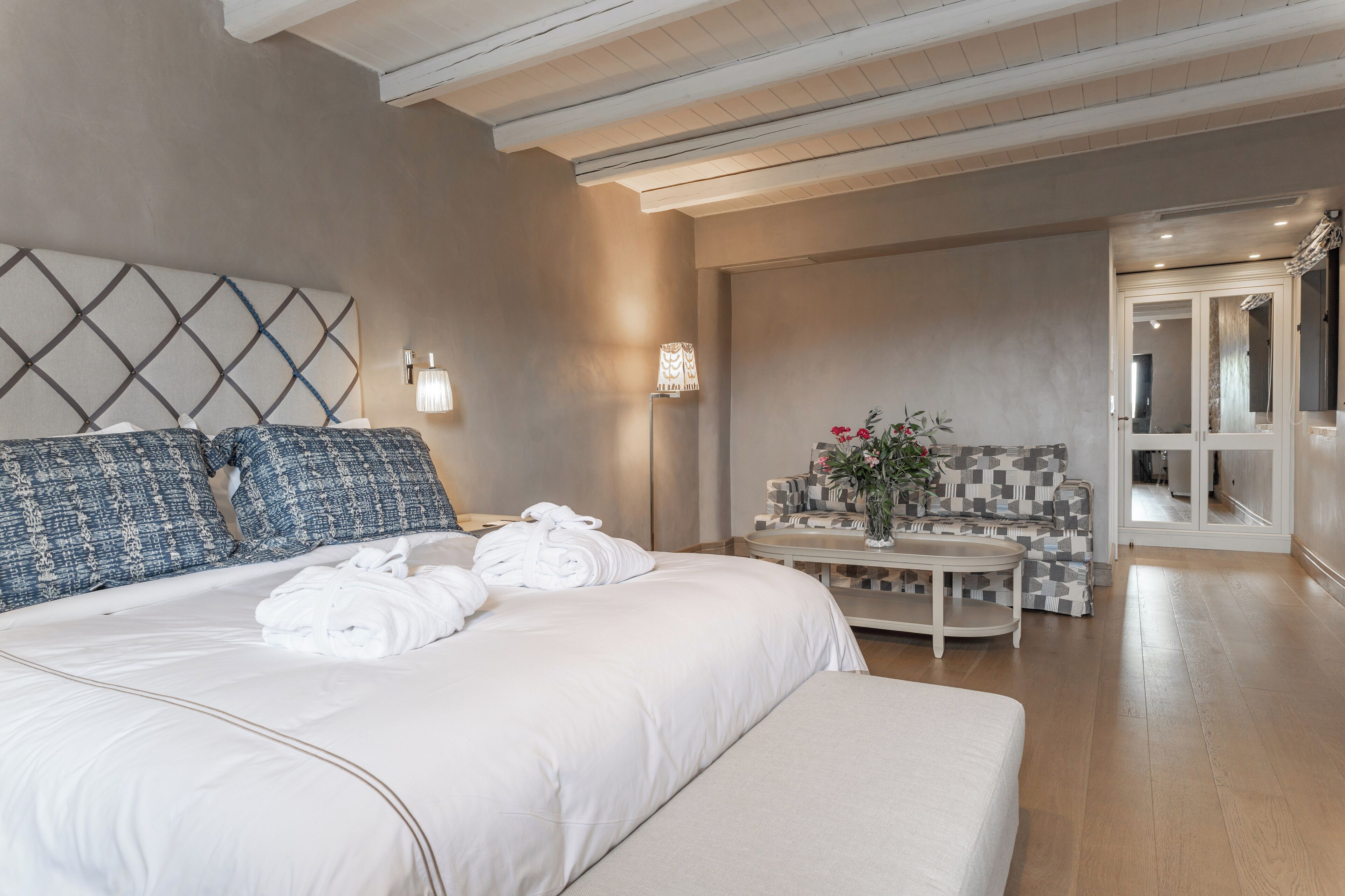 Ein Hotelzimmer mit einem großen Bett, einem Sofa, einem kleinen Tisch mit Blumen und einem Spiegel in der Ecke.