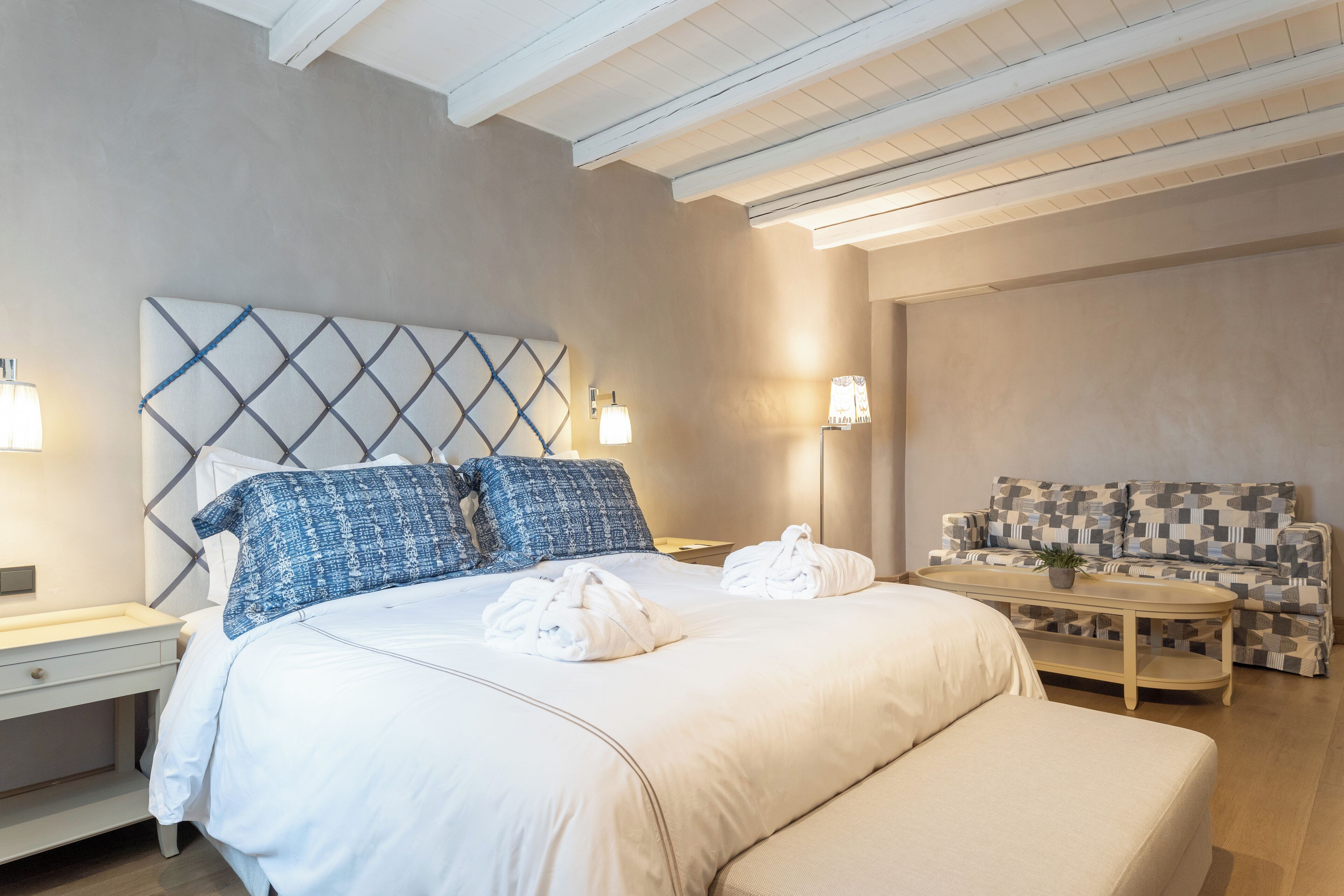 Habitación de hotel con cama, sofá, mesita de noche y una mesa con lámpara.