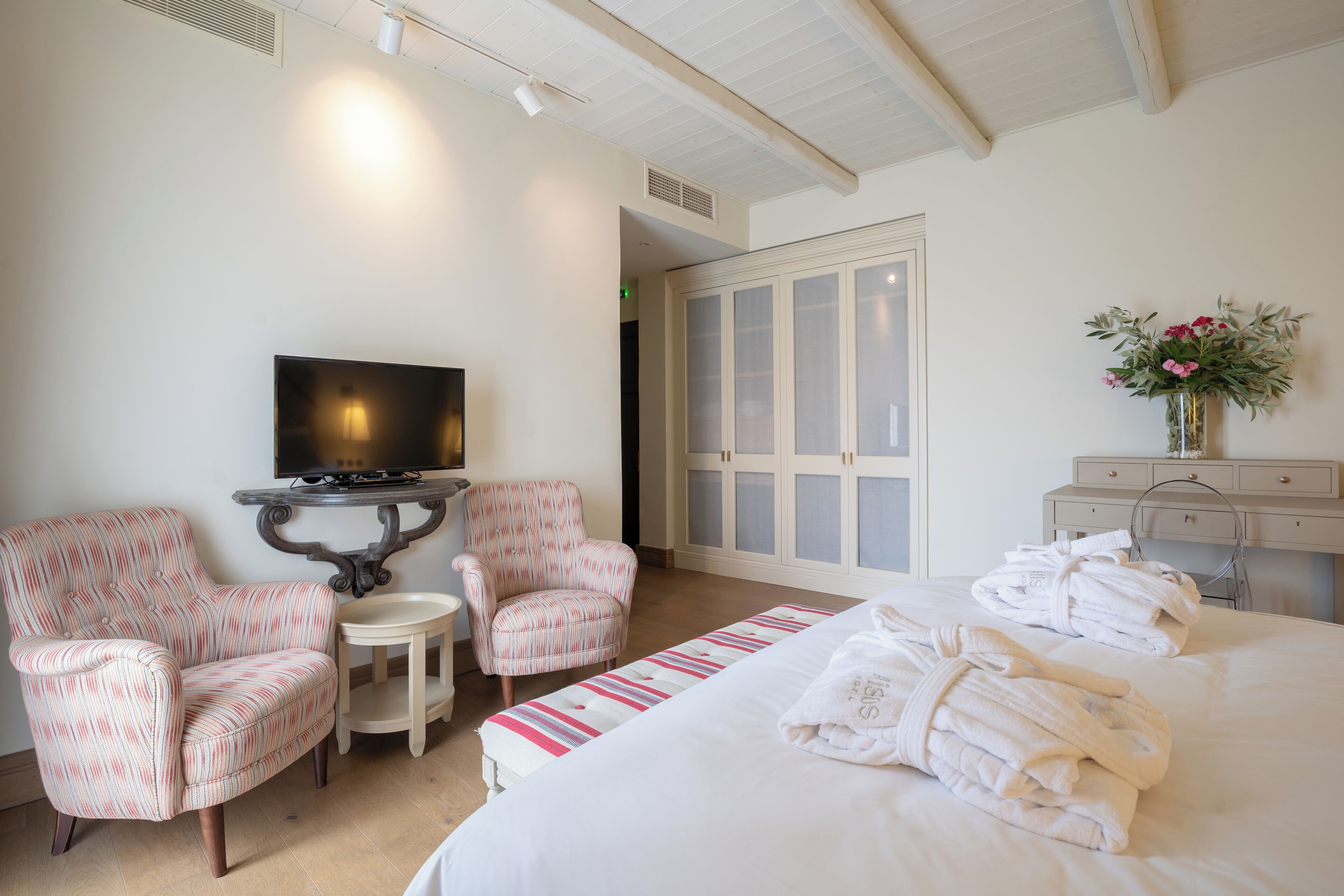 A hotel room with a bed, two armchairs, a small table, a television, and a wardrobe.