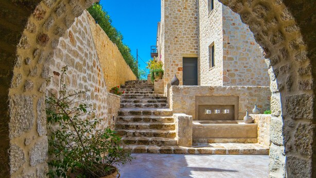 Un sendero de piedra arqueado que conduce a un edificio con fachada de piedra y una puerta.