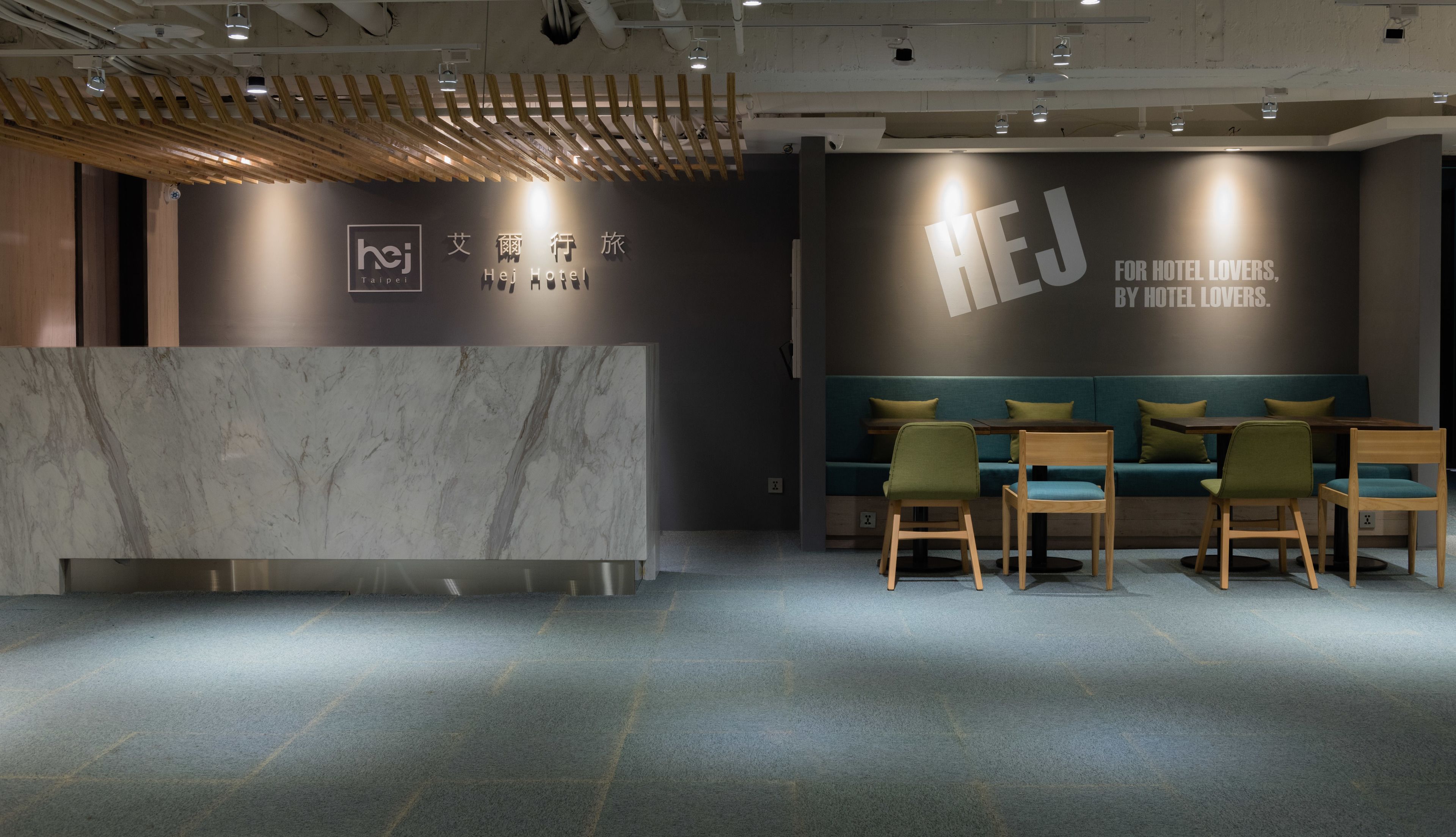 A hotel reception area with a marble counter, wooden ceiling beams, and teal seating.