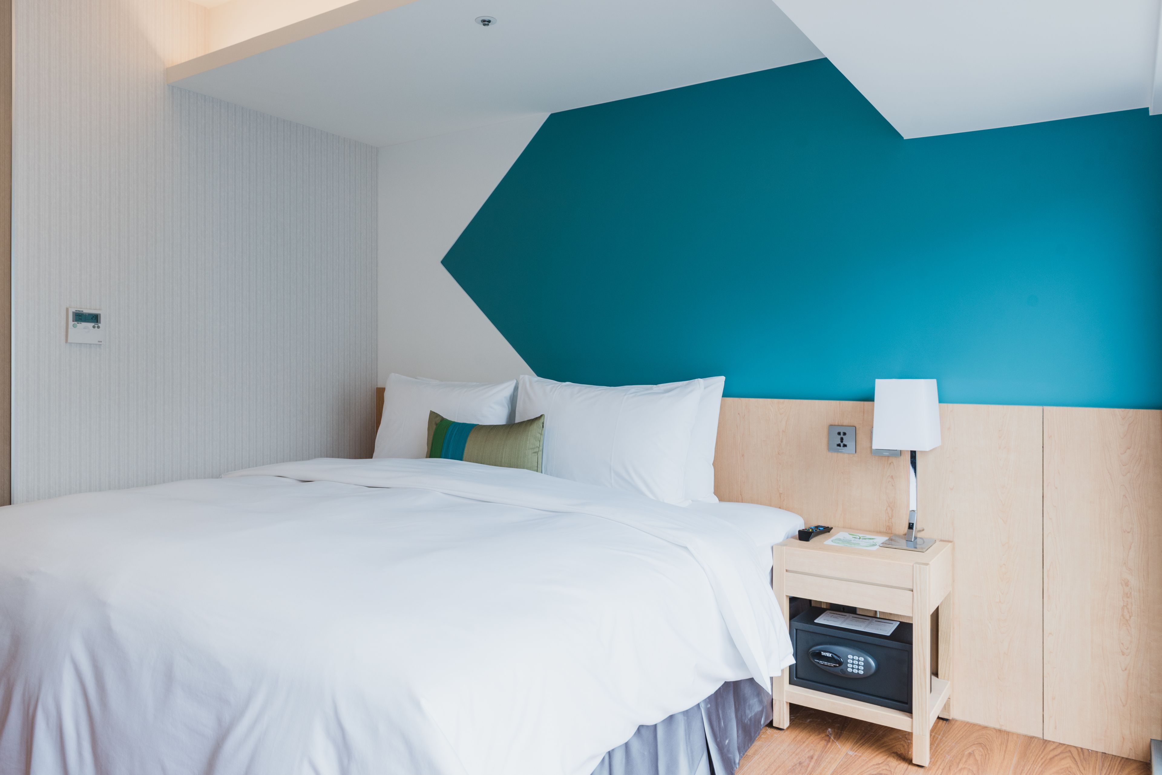 A modern hotel room with a large bed, a nightstand with a lamp, and a wooden headboard.