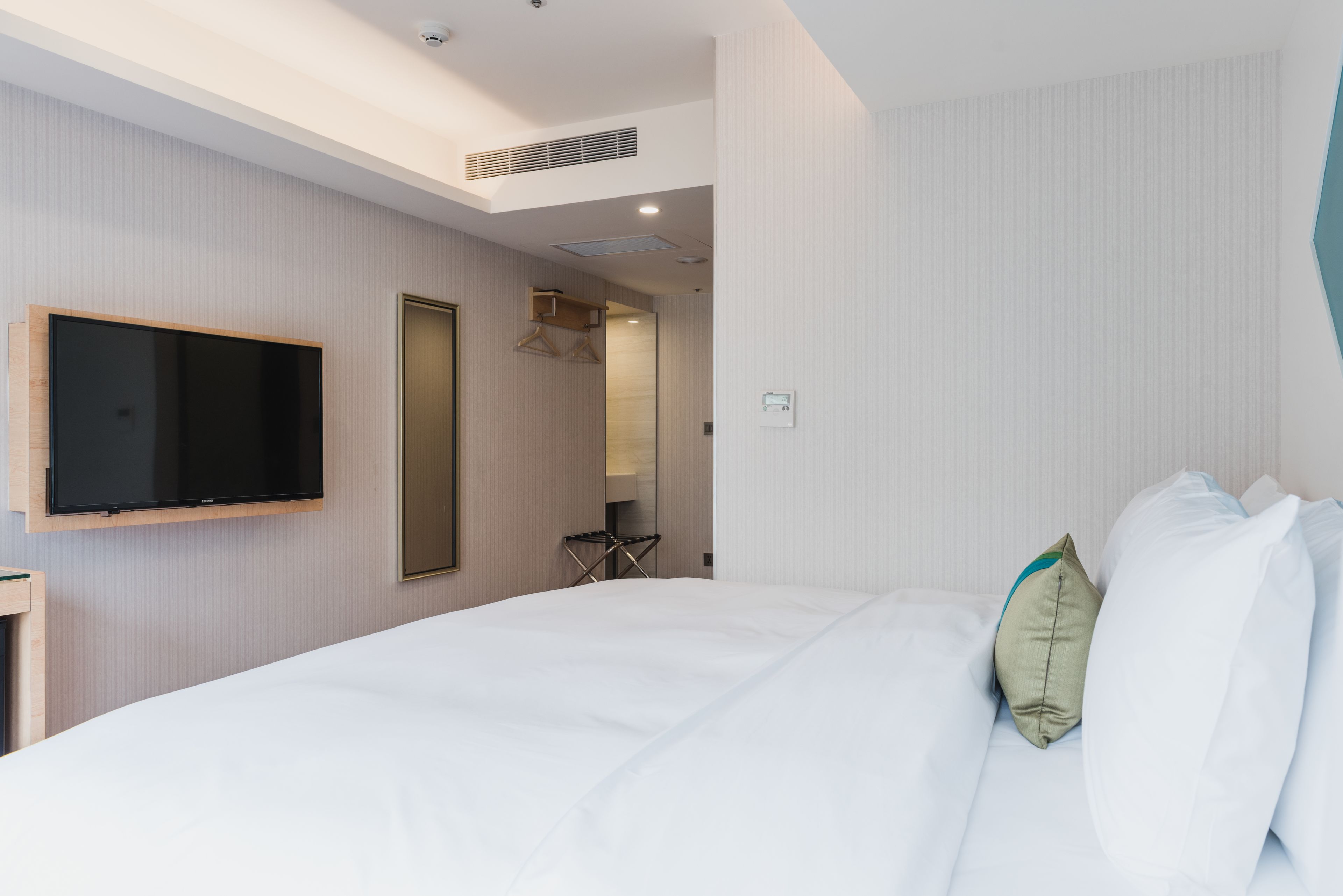 A hotel room with a large bed, a mounted TV, a mirror, and a small seating area.