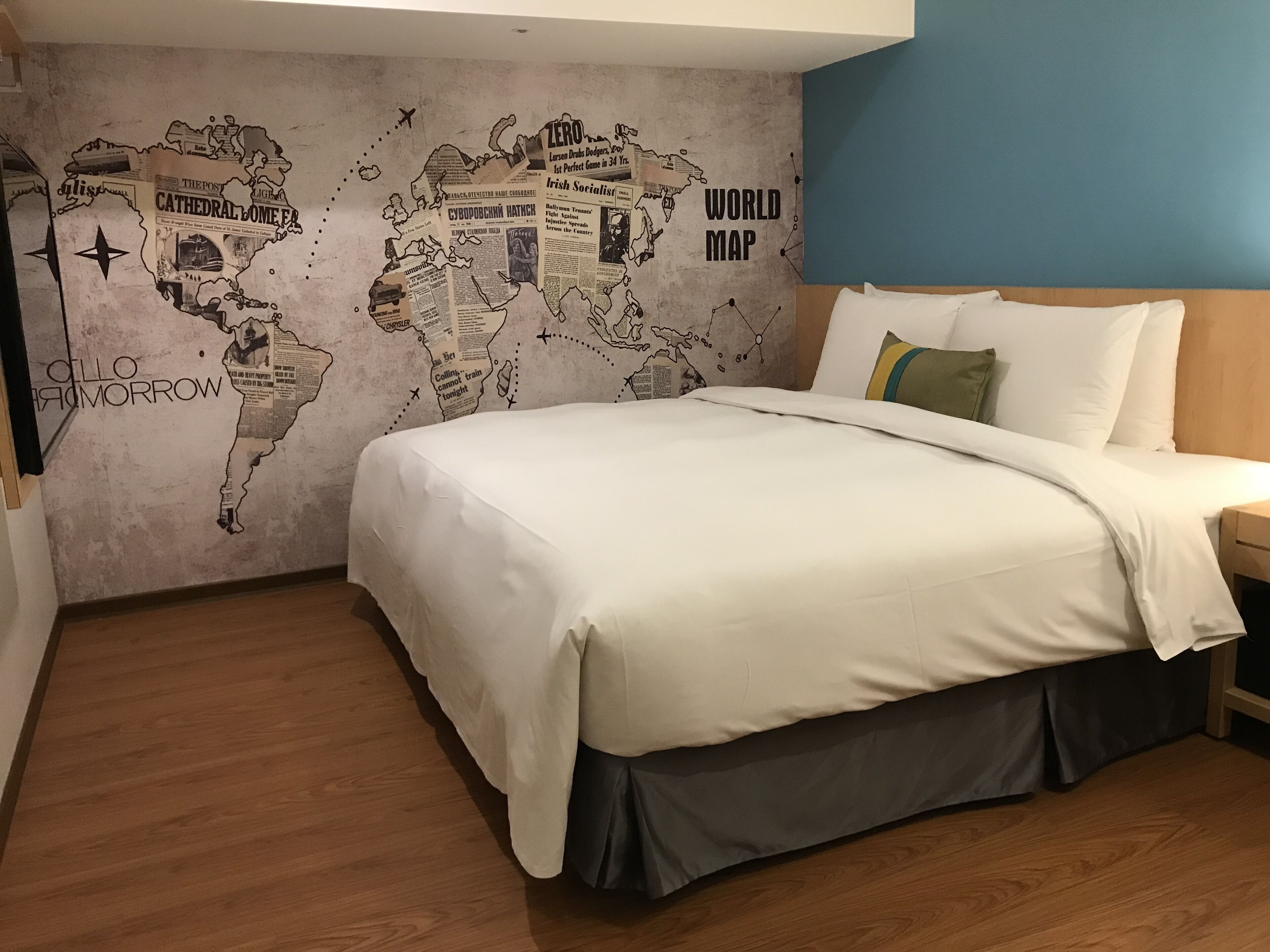 Un dormitorio con un mural de un mapa mundial en la pared, una cama con ropa blanca y suelo de madera.