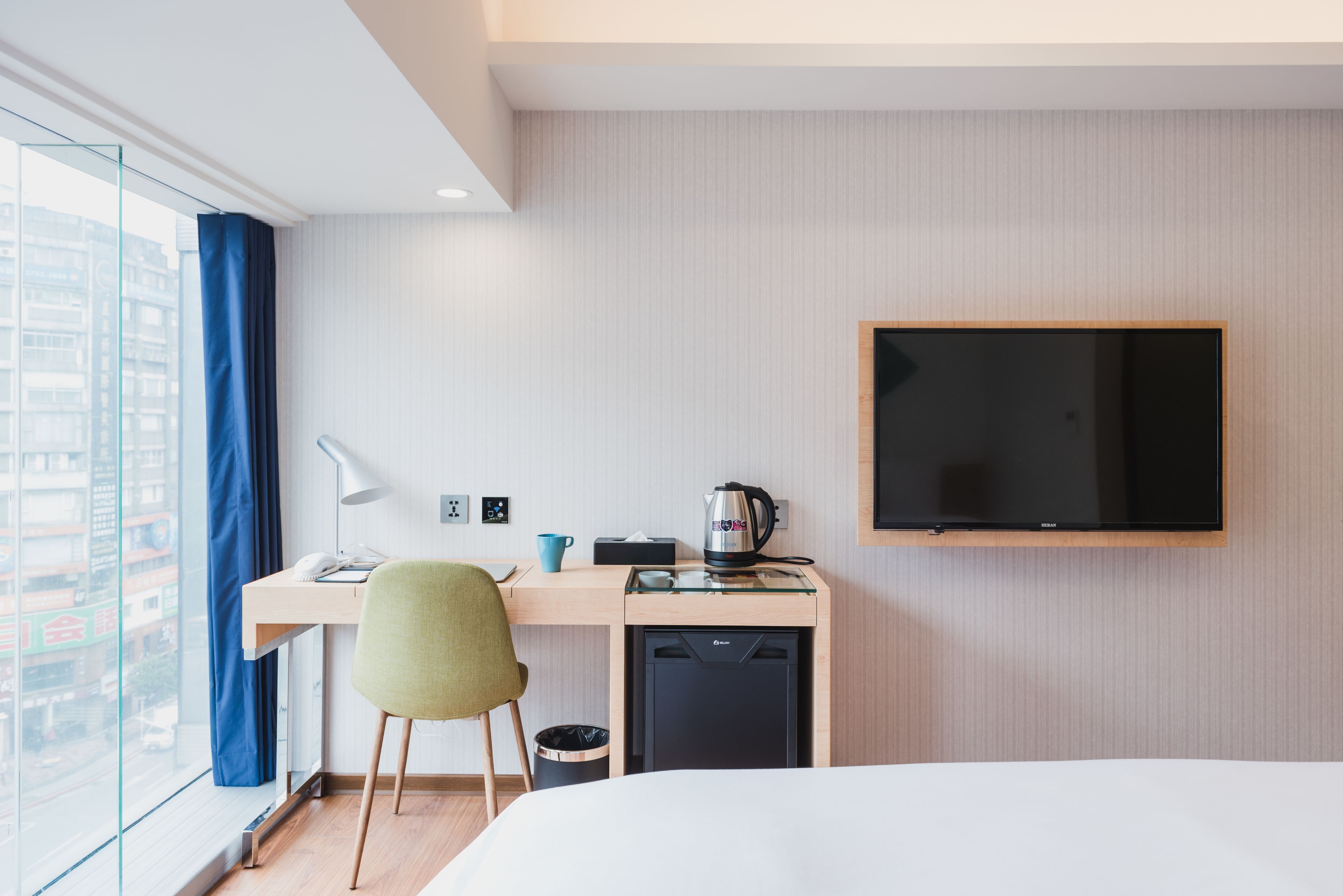 A hotel room with a bed, a desk with a computer, a television, and a small kitchenette.