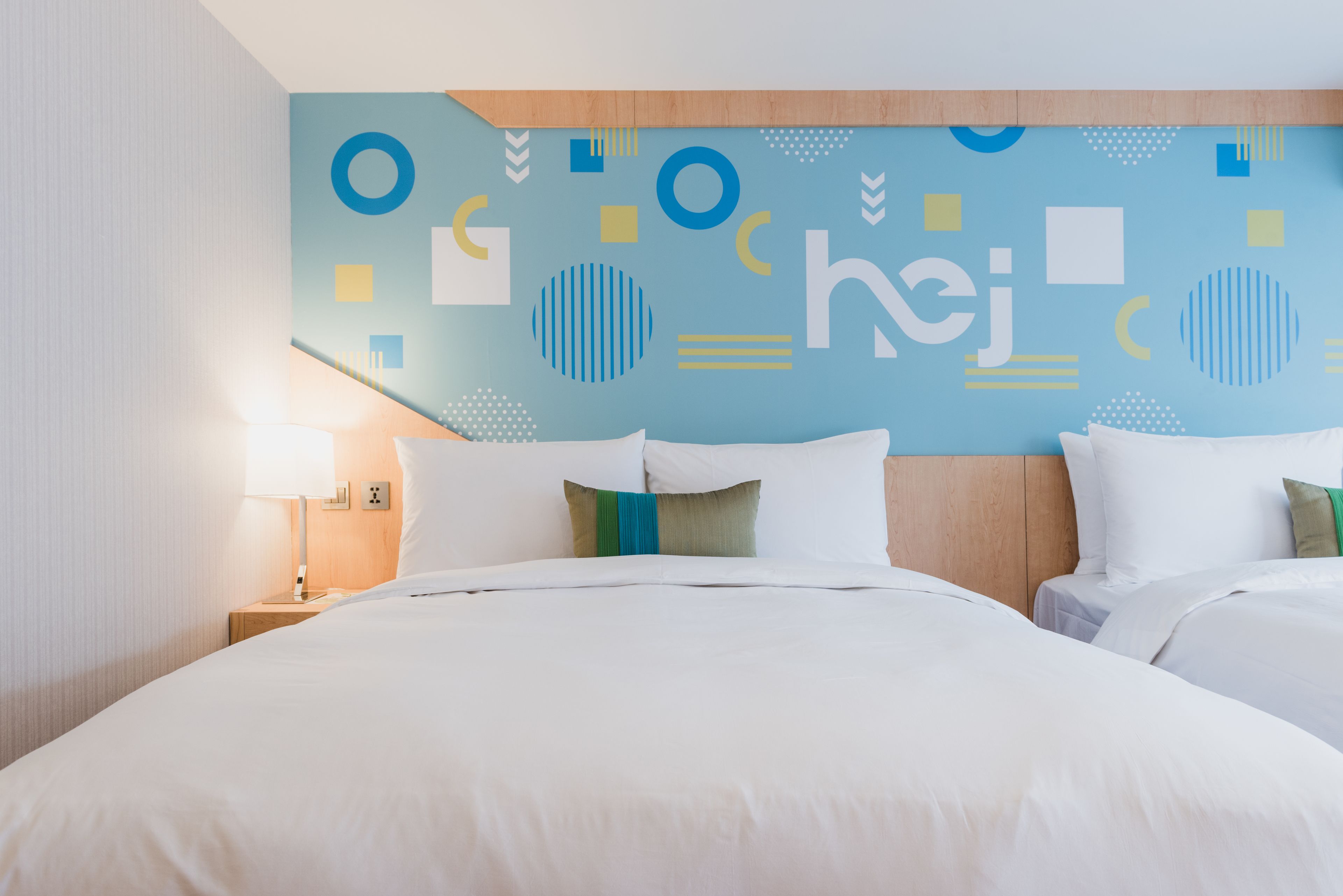 Una habitació d'hotel amb un llit gran, una tauleta de nit, una làmpada i una paret amb dibuixos geomètrics.