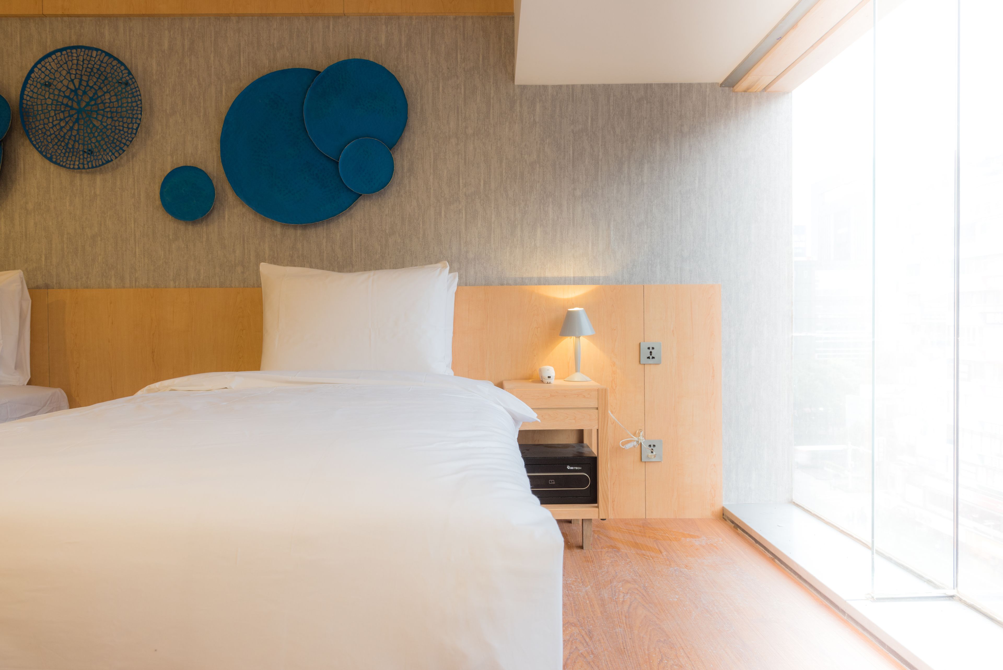 Una habitación de hotel moderna con una cama grande, una mesita de noche con lámpara y una pared con arte abstracto azul.
