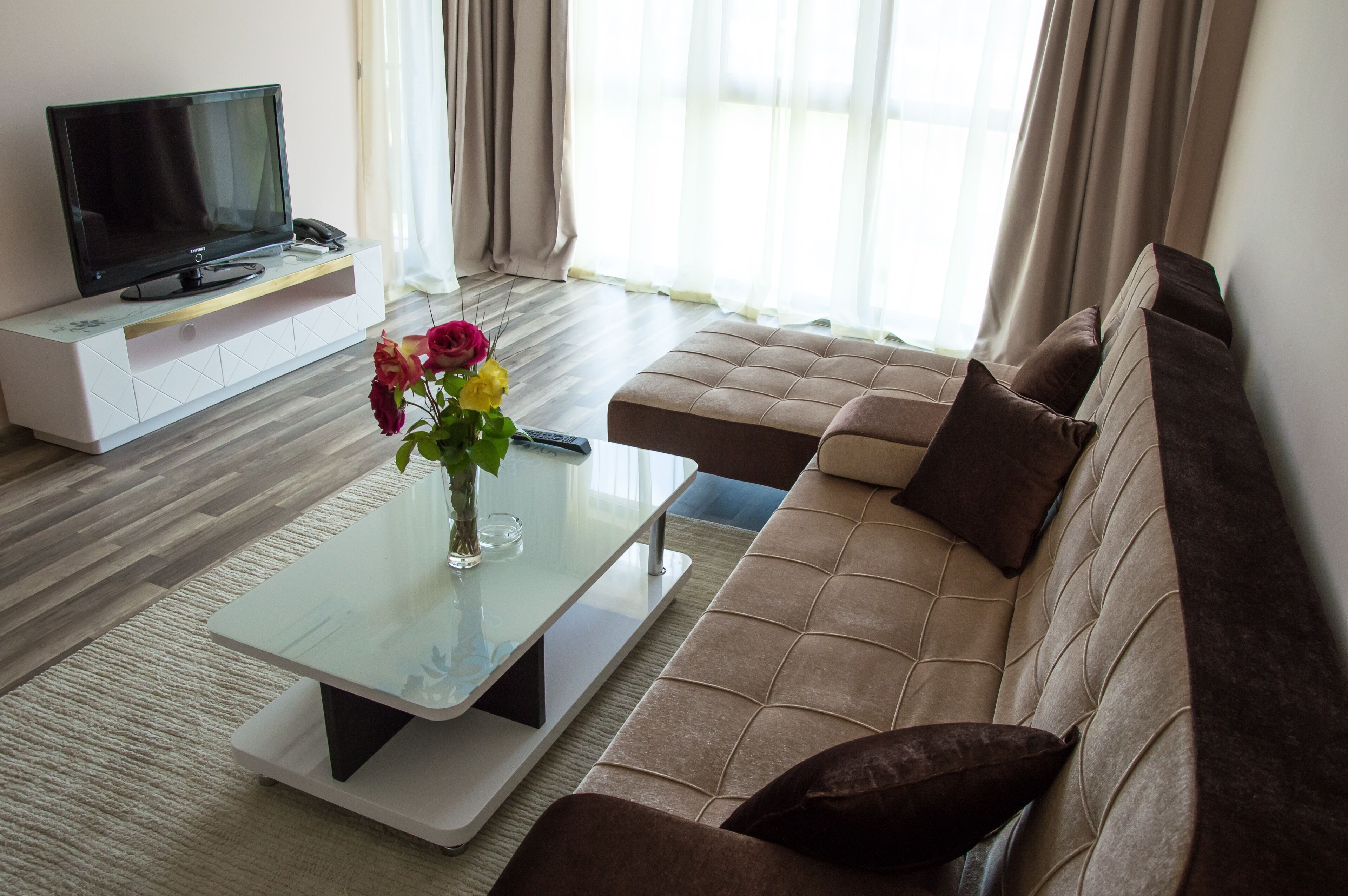 A modern living room with a sofa, a glass coffee table, a TV on a stand, and a vase with flowers.