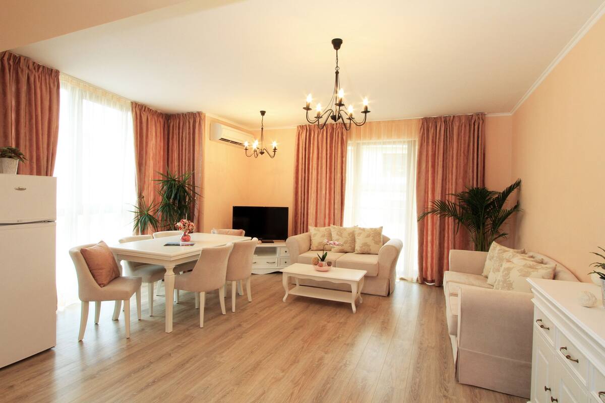 A modern living room with a dining area, a sofa, a TV, and a chandelier.