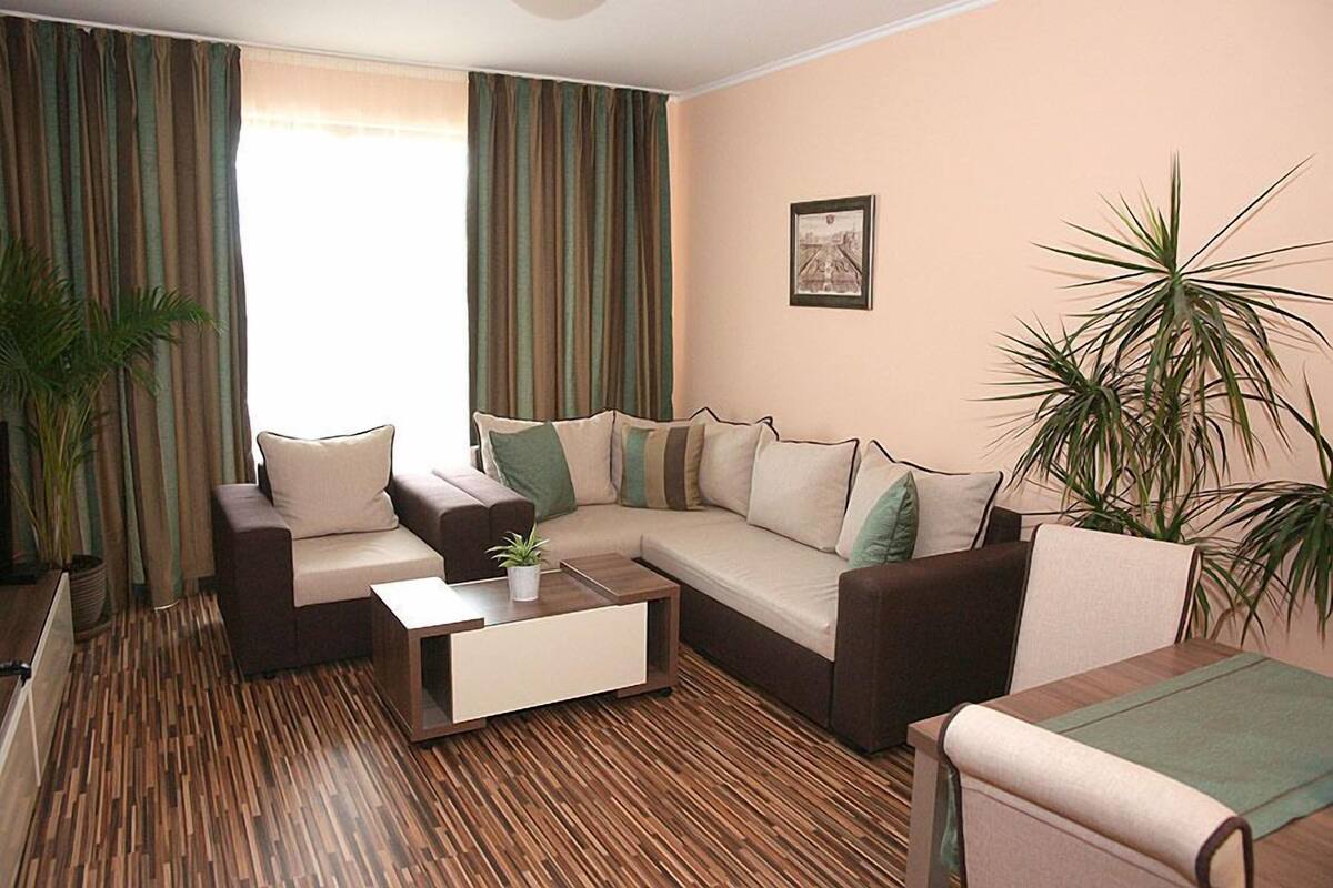 A living room with a sectional sofa, a coffee table, and two potted plants.