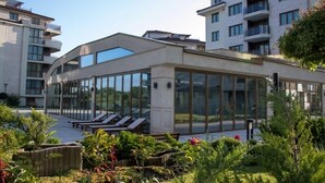 A modern building with large glass windows, a rooftop terrace with sun loungers, and a well-maintained garden area. - Long Beach Resort & Spa (Dolni Chiflik)