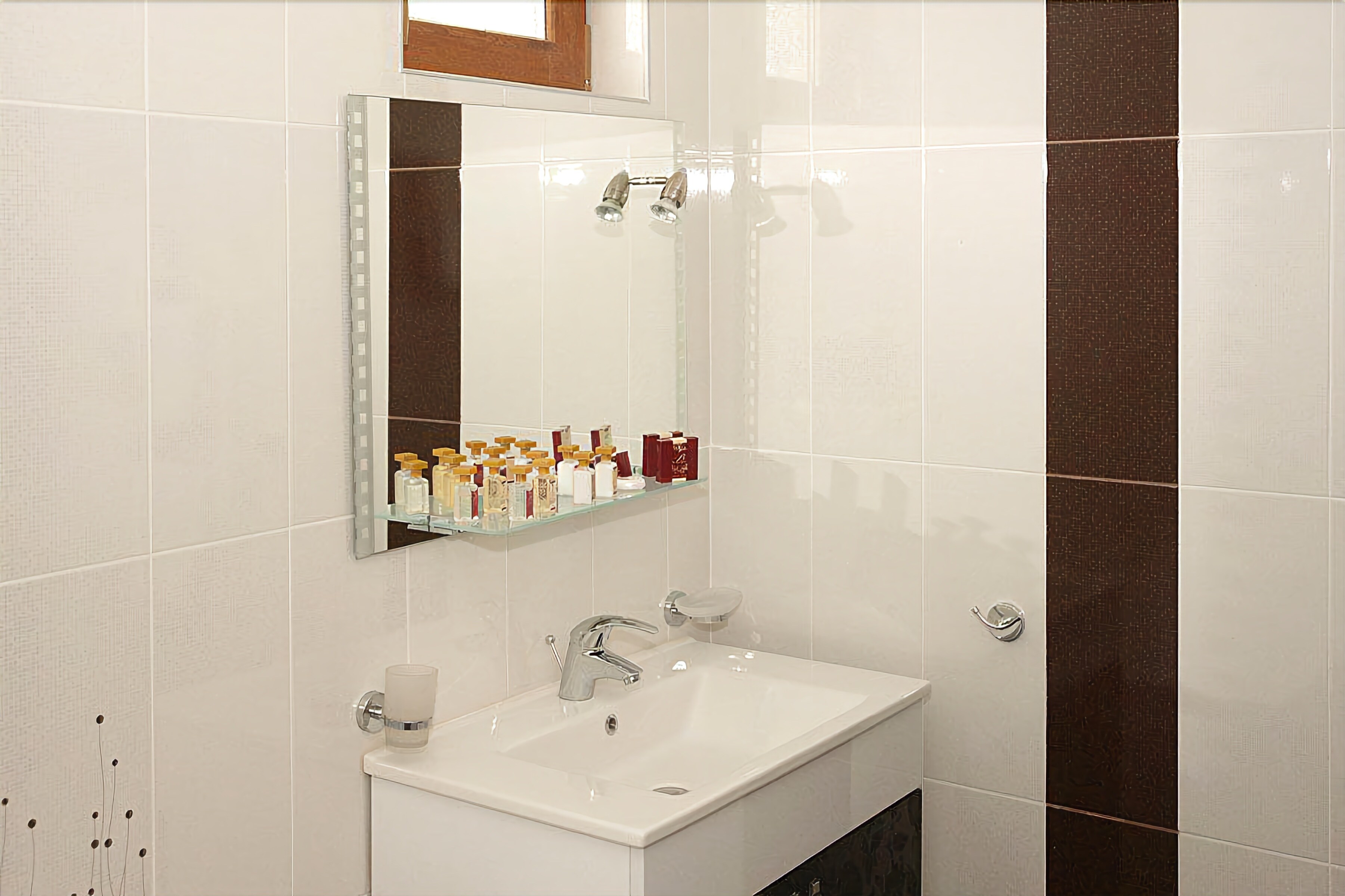 A bathroom with a white sink, mirror, and shower. There are toiletries on a shelf above the sink.