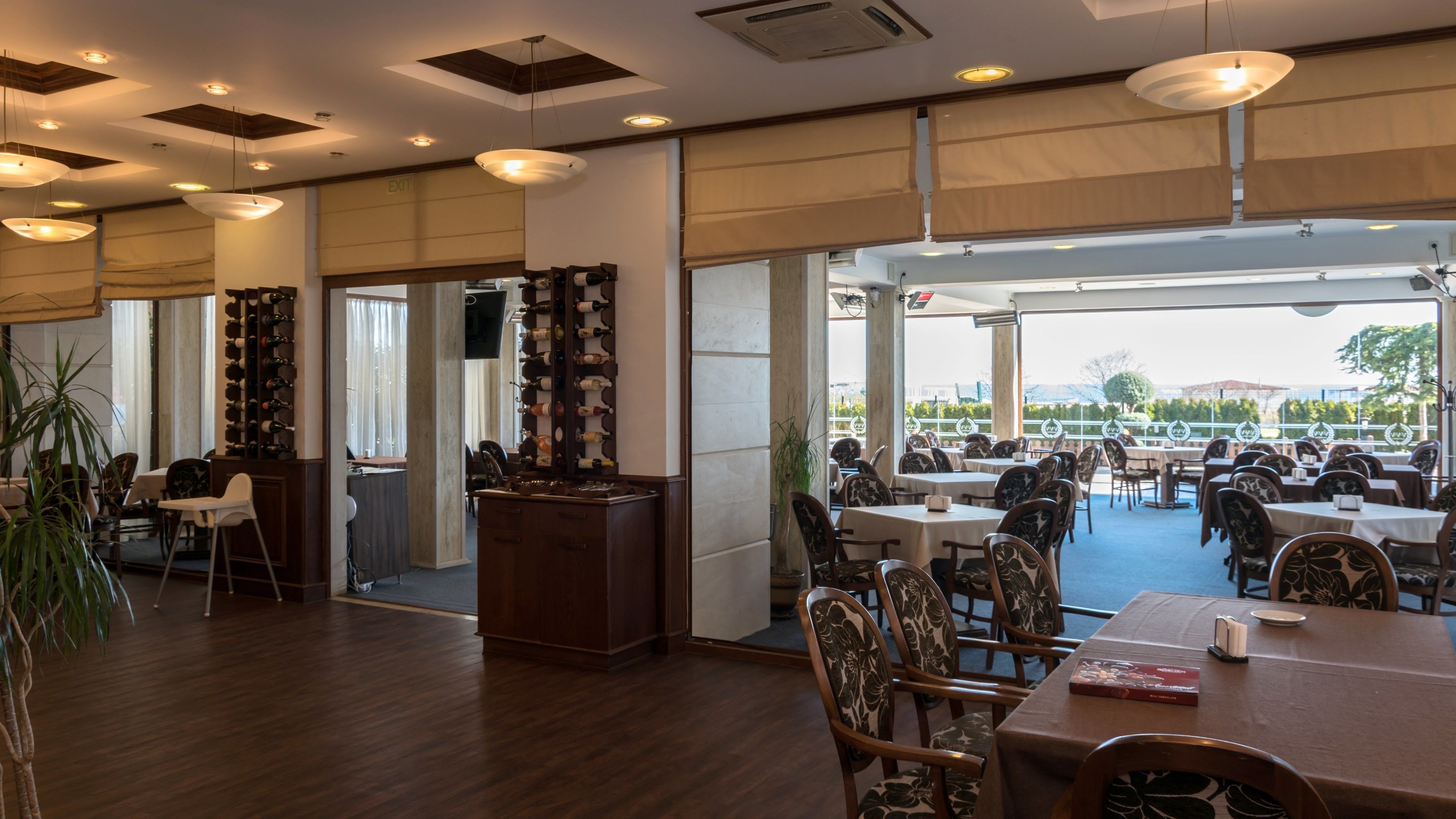 Een restaurant met meerdere eettafels en stoelen, een wijnrek en uitzicht op het omliggende landschap.