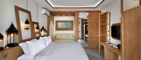 A modern bedroom with a large bed, bedside lamps, a painting, a sofa, and a TV.