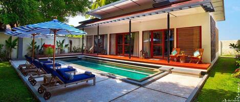 Una casa moderna con piscina, sillas de sol y un porche cubierto.